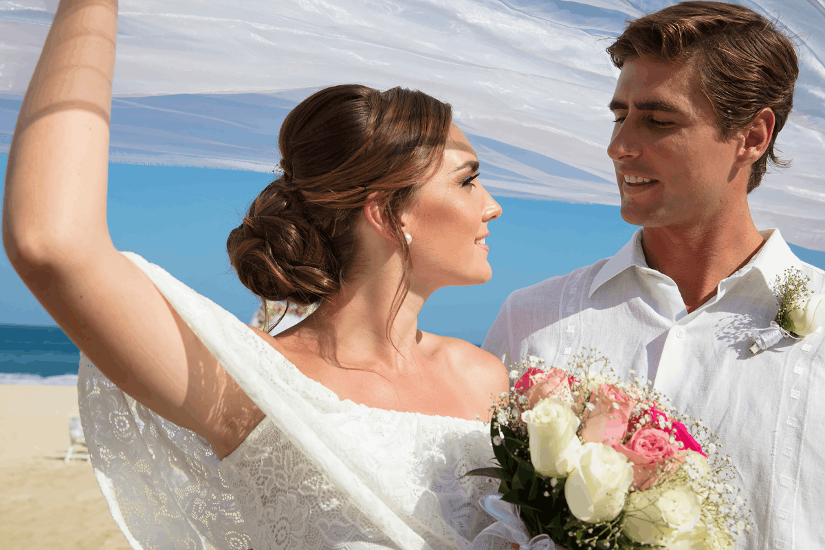 Pareja celebrando su boda en Krystal Grand Los Cabos con ramo floral, vestimenta blanca y paisaje frente al mar.